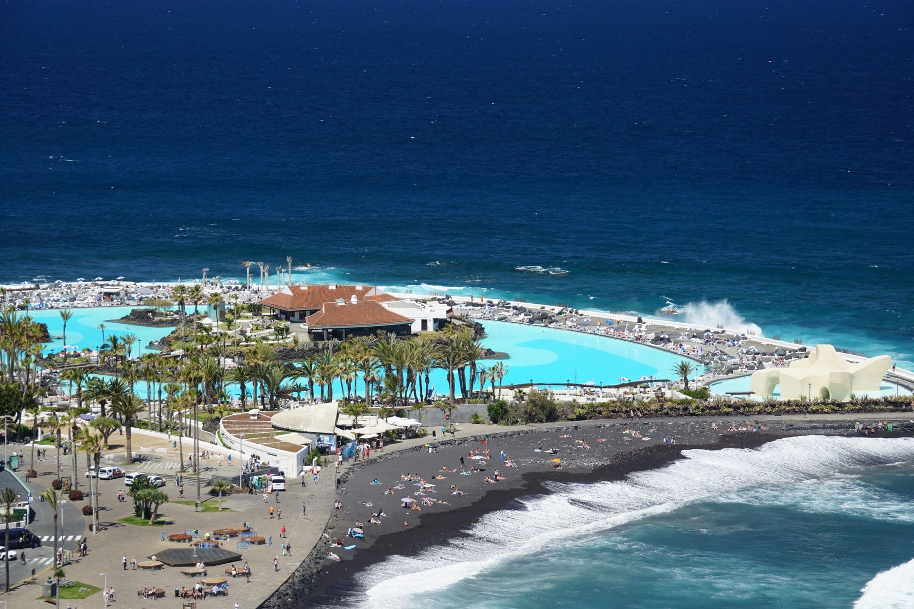 A stunning aerial shot of a coastal resort with black sand beach and blue ocean in Tenerife.
