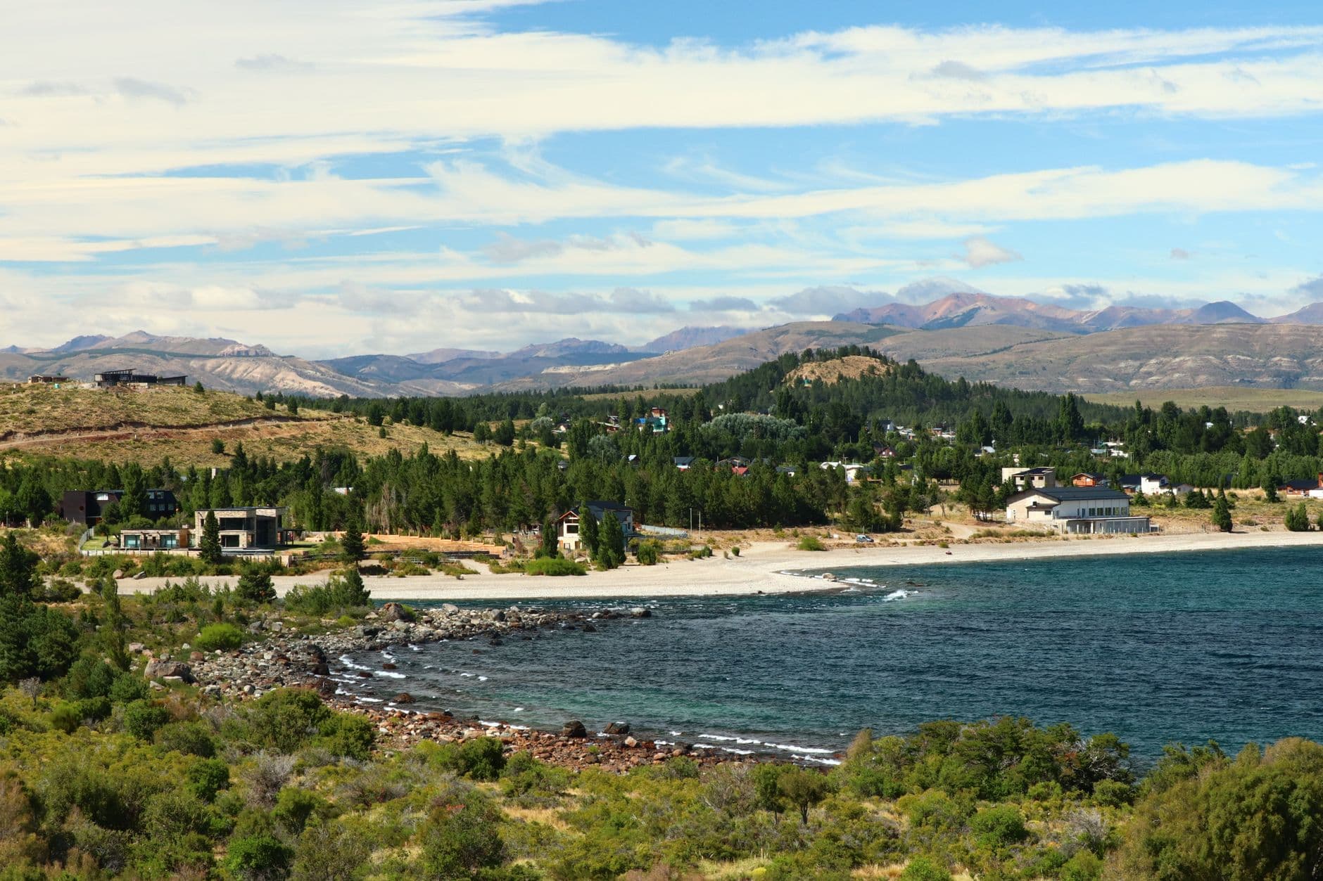 Breathtaking view of a coastal landscape with trees and mountains in the background under a blue sky.