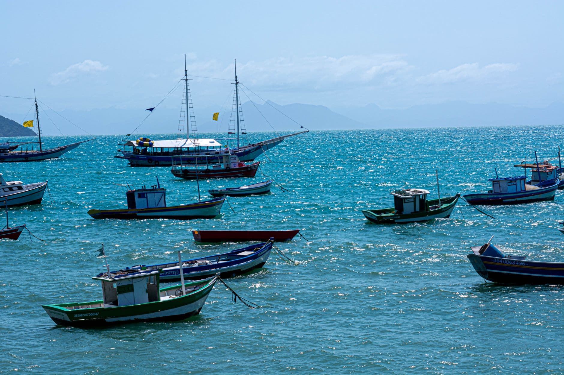 Colorful boats anchored in the vibrant blue waters of Armação dos Búzios, Brazil.