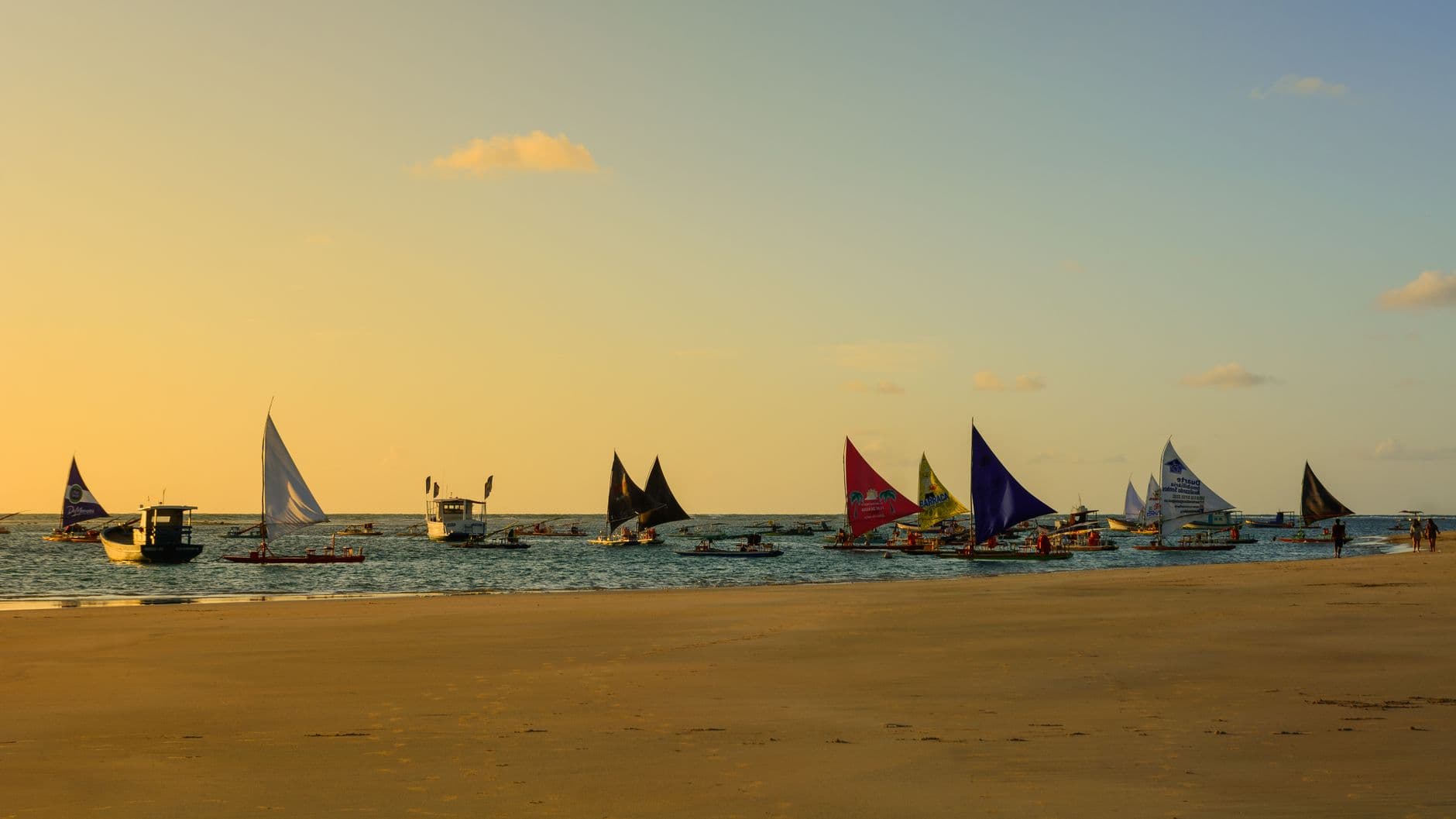 Vibrant sailboats on Porto de Galinhas beach during sunset in Brazil.