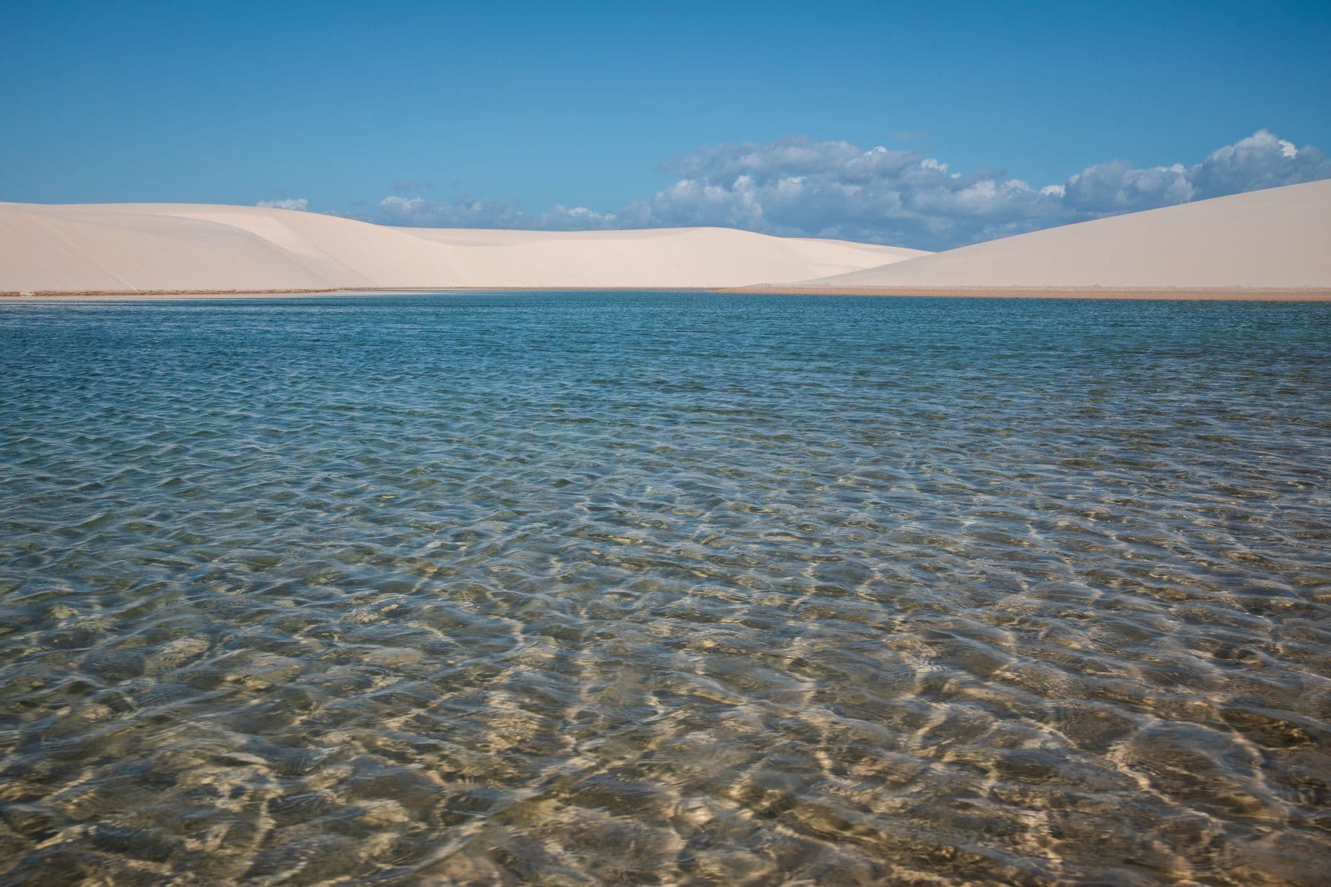 A stunning landscape of sand dunes and a pristine lagoon in Lençóis Maranhenses, Brazil.