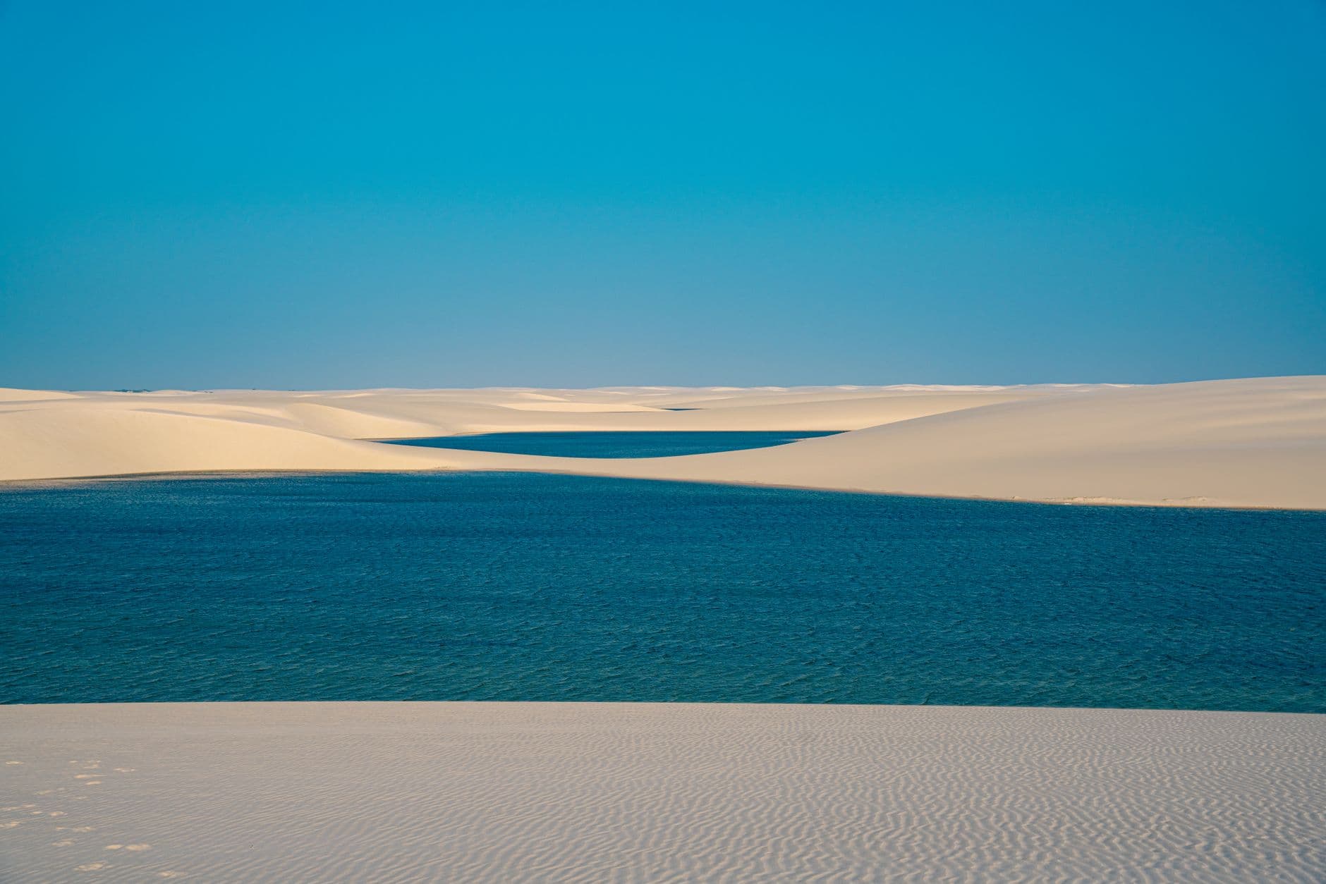 Captivating view of clear blue waters amidst sandy dunes under a bright sky, resembling a desert oasis.