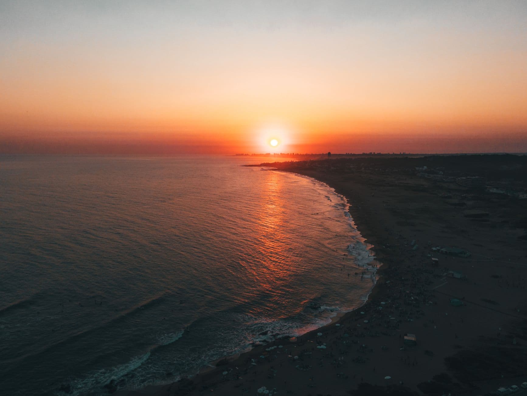 A breathtaking aerial view of a sunset over Punta del Este beach, casting warm hues on the ocean waves.