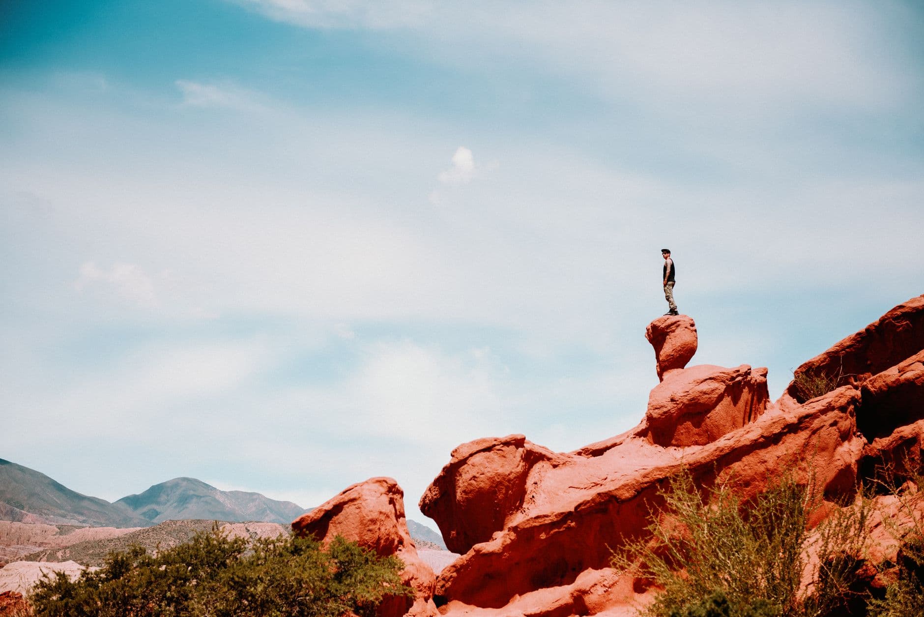Man standing on distinctive red rock formations in Cafayate, Salta, against a blue sky.