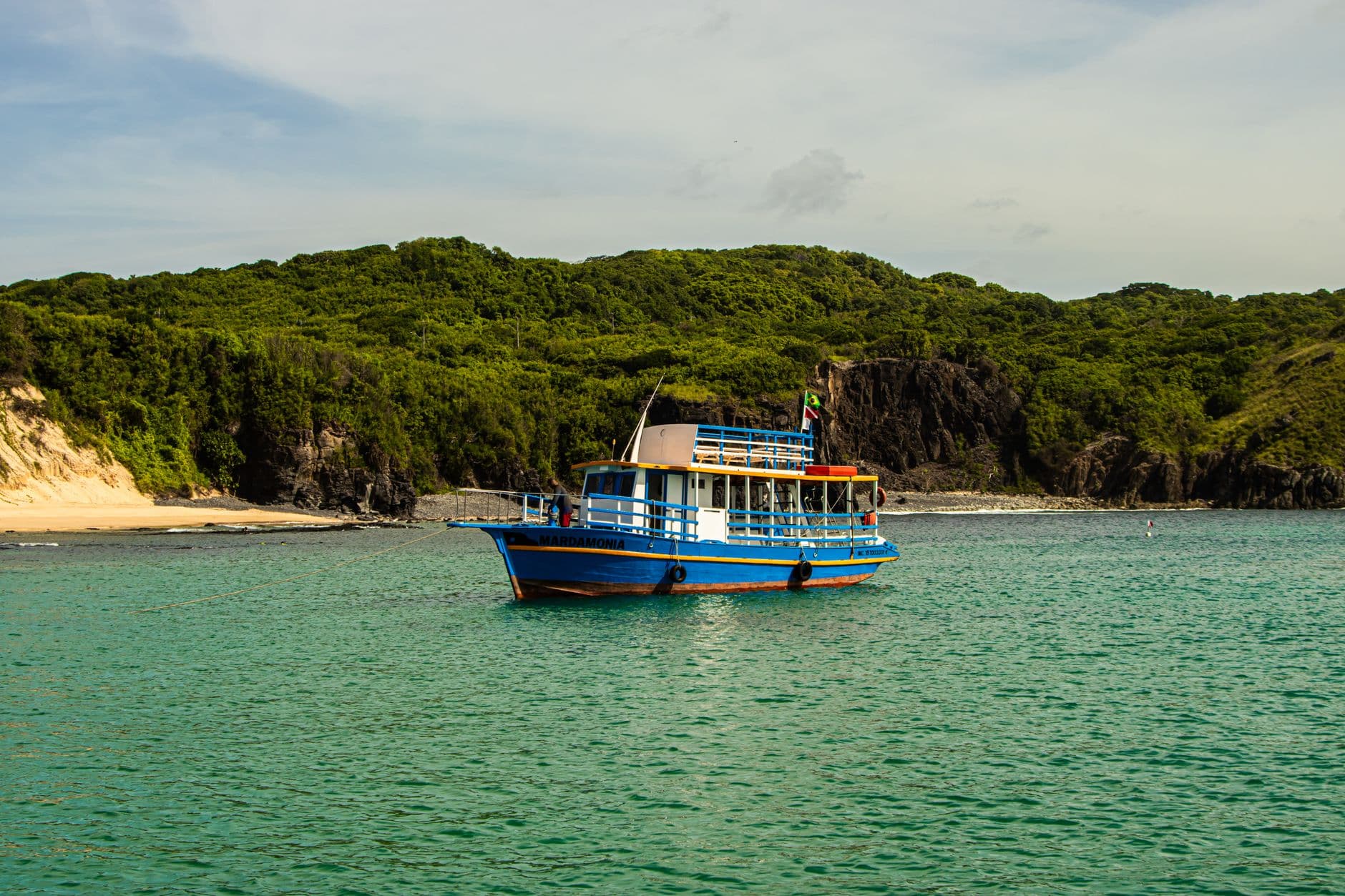 Colorful boat on serene tropical waters, framed by lush green hills and clear blue skies.