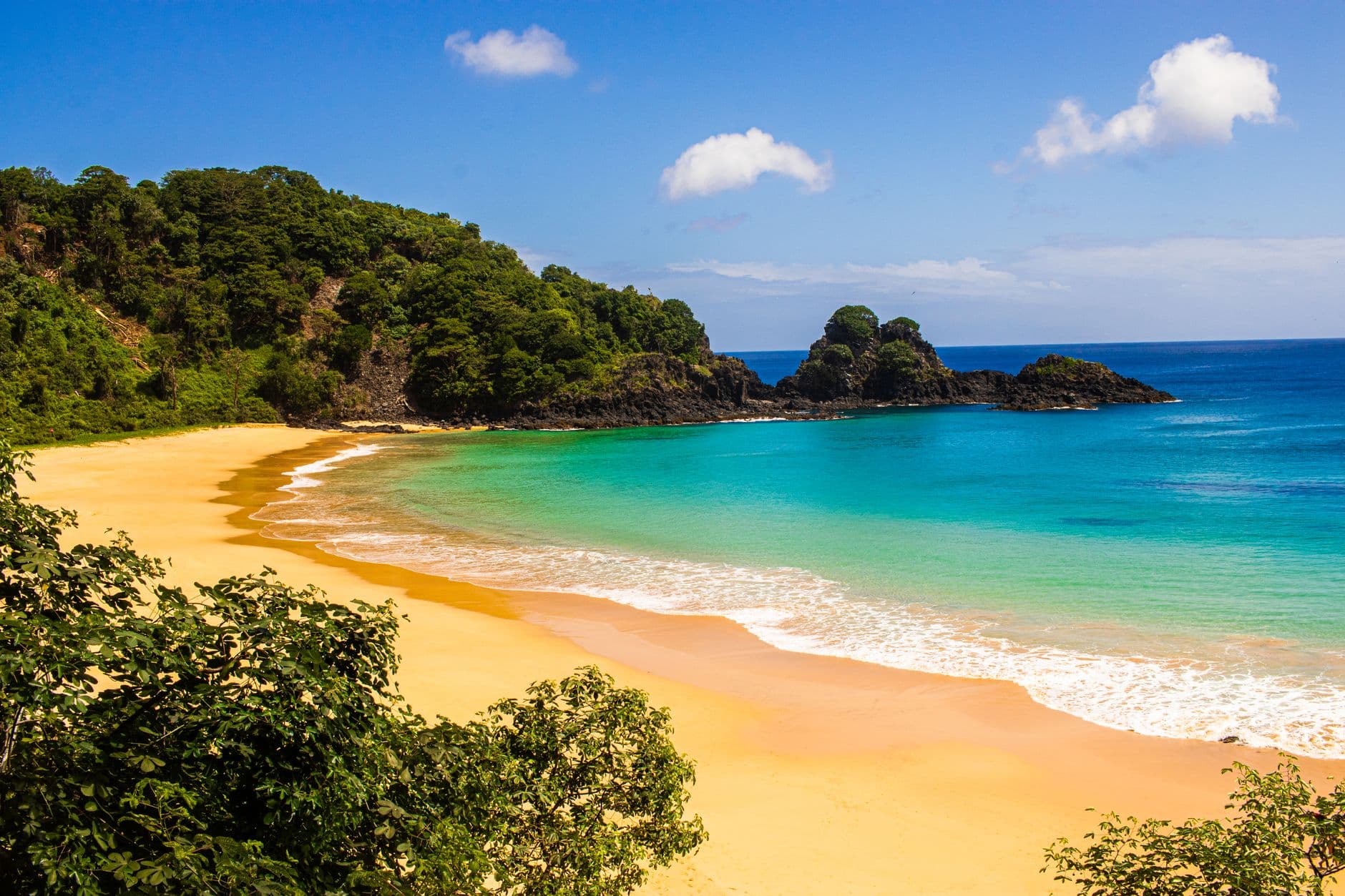 A breathtaking aerial view of a clear turquoise bay in Brazil with a boat and lush cliffs.