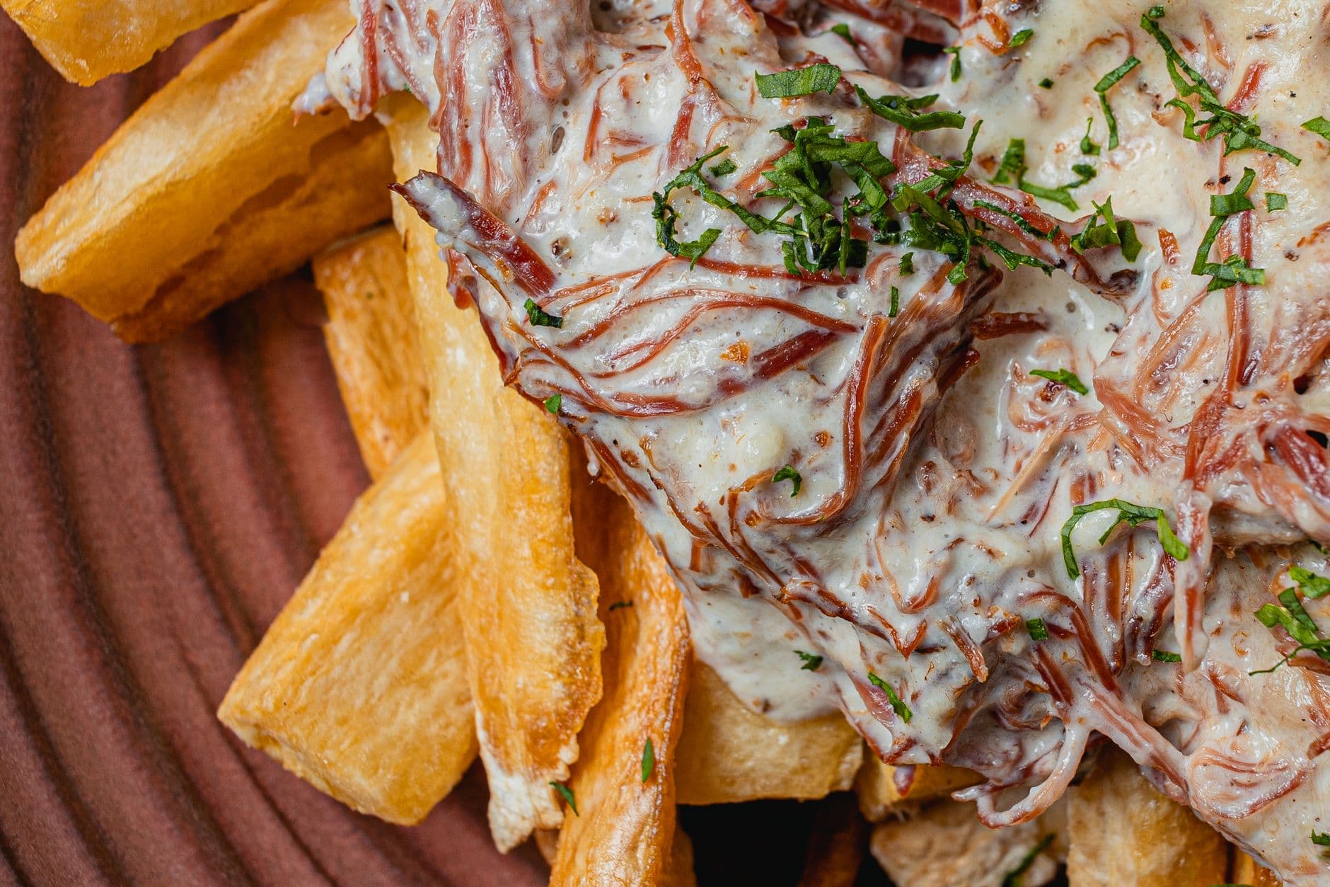 Close-up of Brazilian carne de sol with creamy sauce served on crispy cassava fries. A Maceió culinary delight.