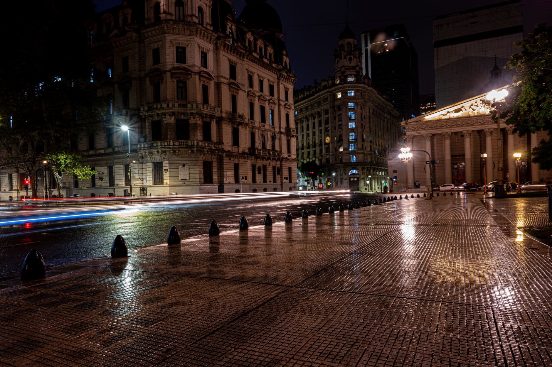 Illuminated historic architecture in Buenos Aires during nighttime with street lights reflecting on wet pavement.