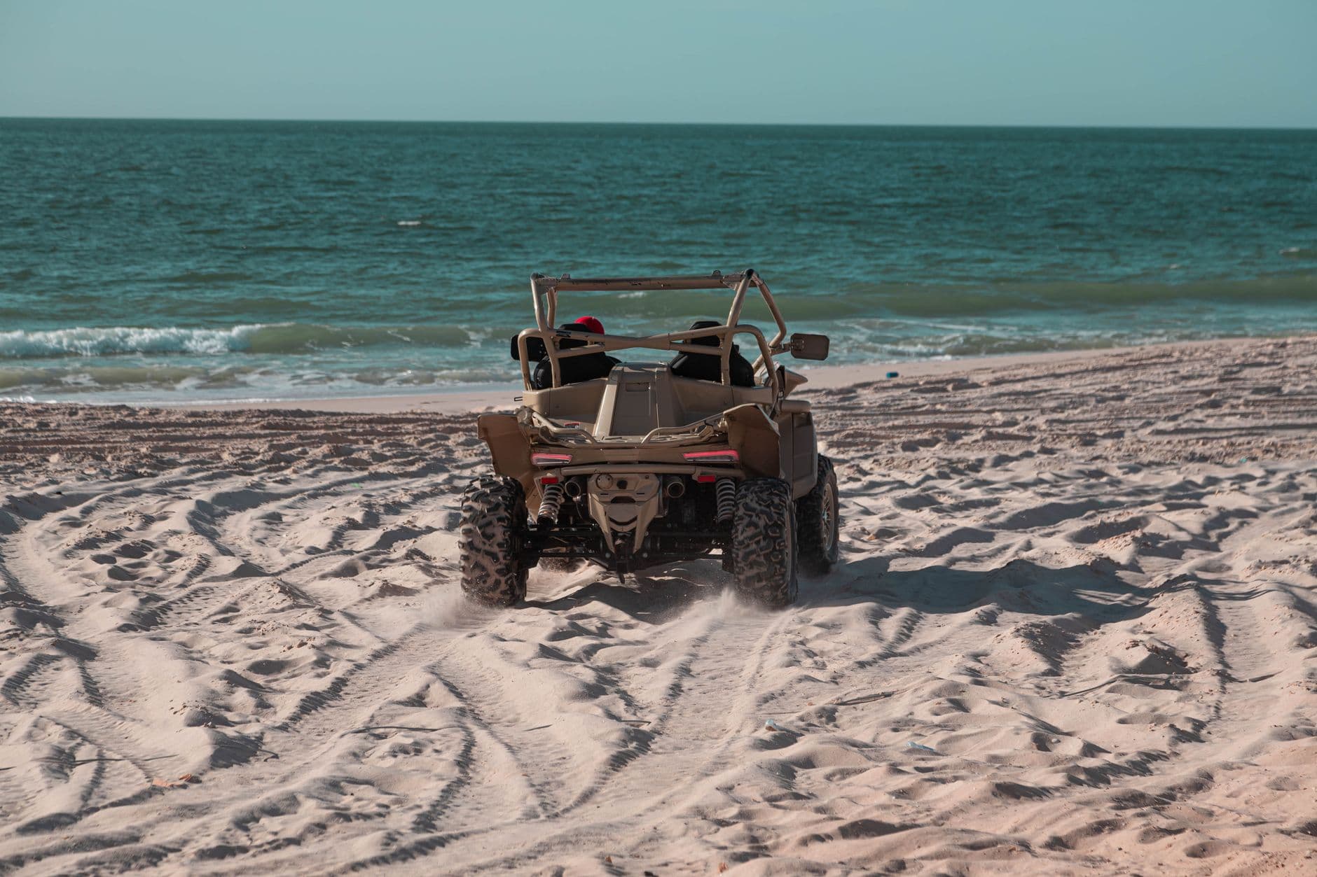 Beach buggy driving on sandy shore near ocean waves, perfect for summer adventures.